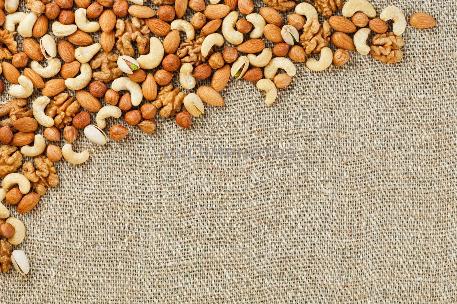 Mix of nuts of cashew, almonds, pistachios, hazelnuts and walnuts is against the background of brown fabric of burlap. Nuts as structure and background, macro