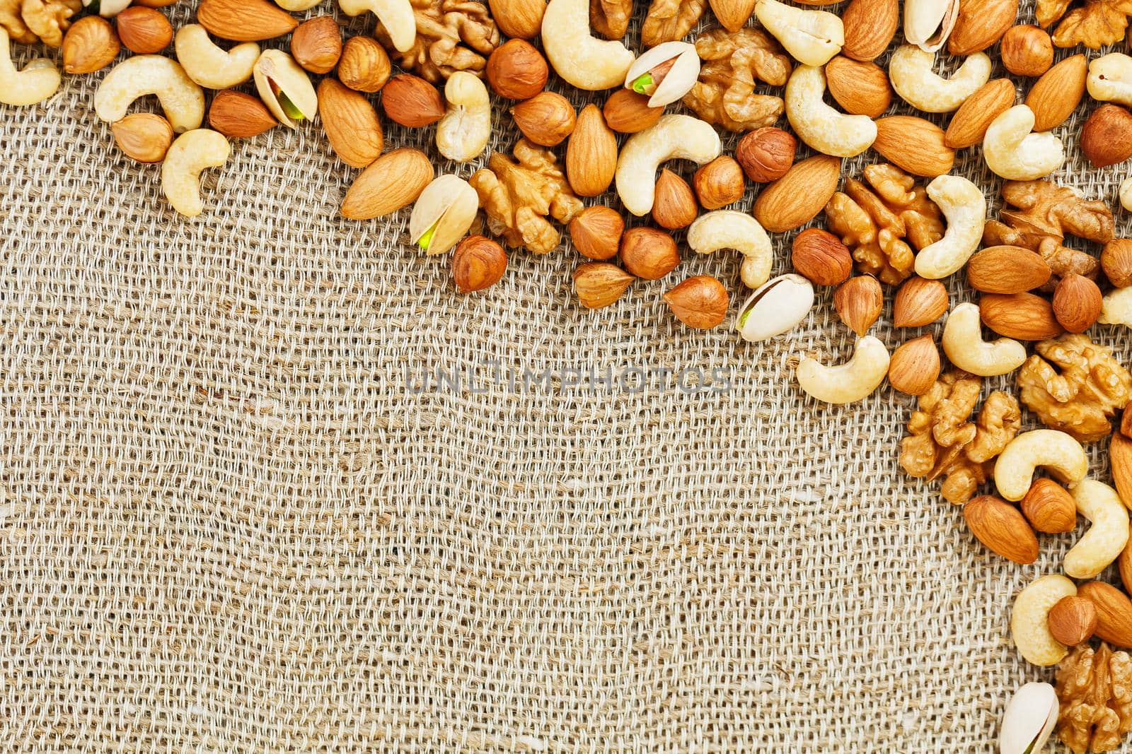 Mix of nuts of cashew, almonds, pistachios, hazelnuts and walnuts is against the background of brown fabric of burlap. Nuts as structure and background, macro