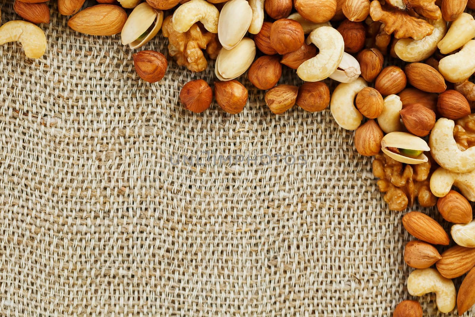 Mix of nuts of cashew, almonds, pistachios, hazelnuts and walnuts is against the background of brown fabric of burlap. Nuts as structure and background, macro