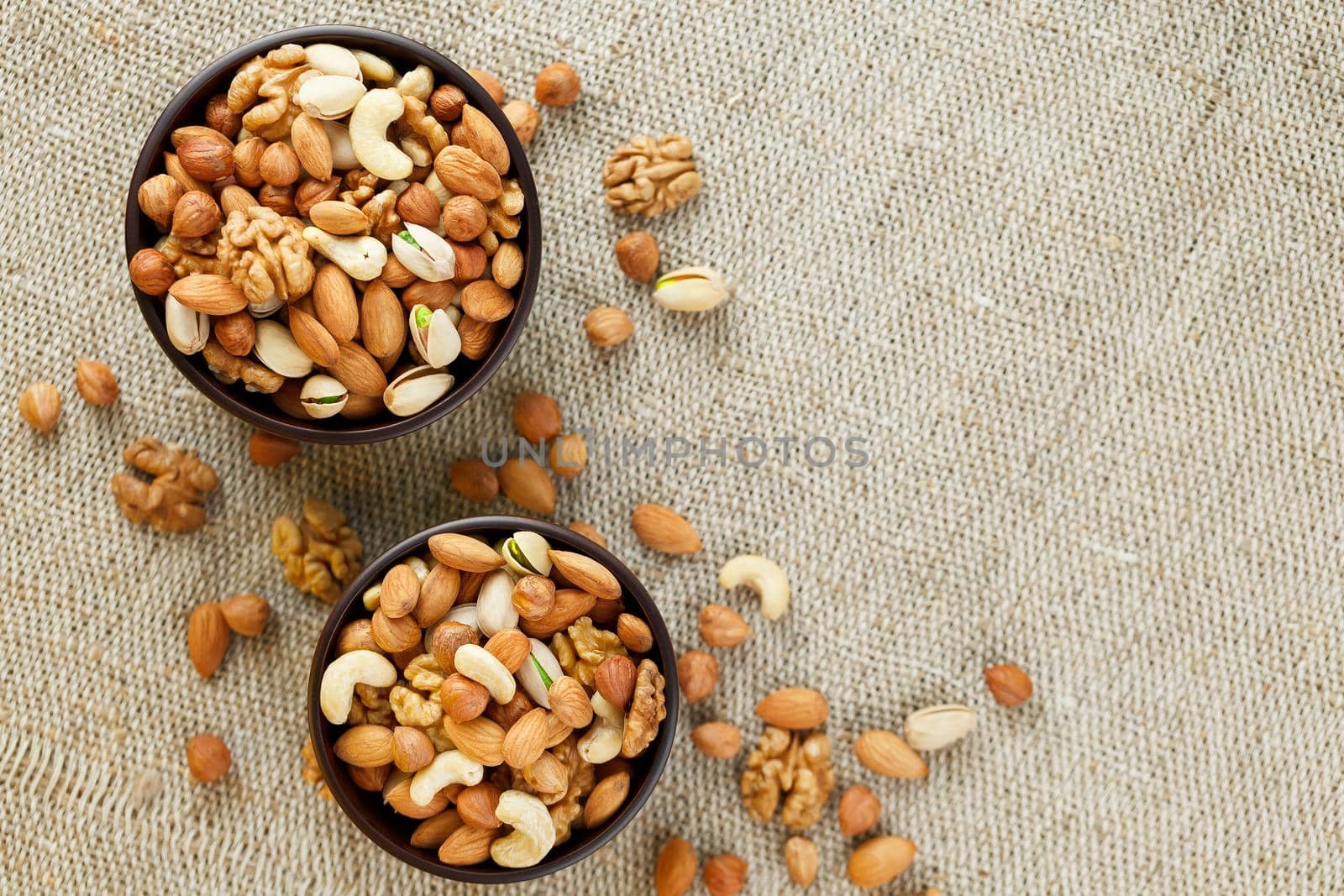 Mix of various nuts in a wooden cup against the background of fabric from burlap. Nuts as structure and background, macro. Top view. by AlexGrec