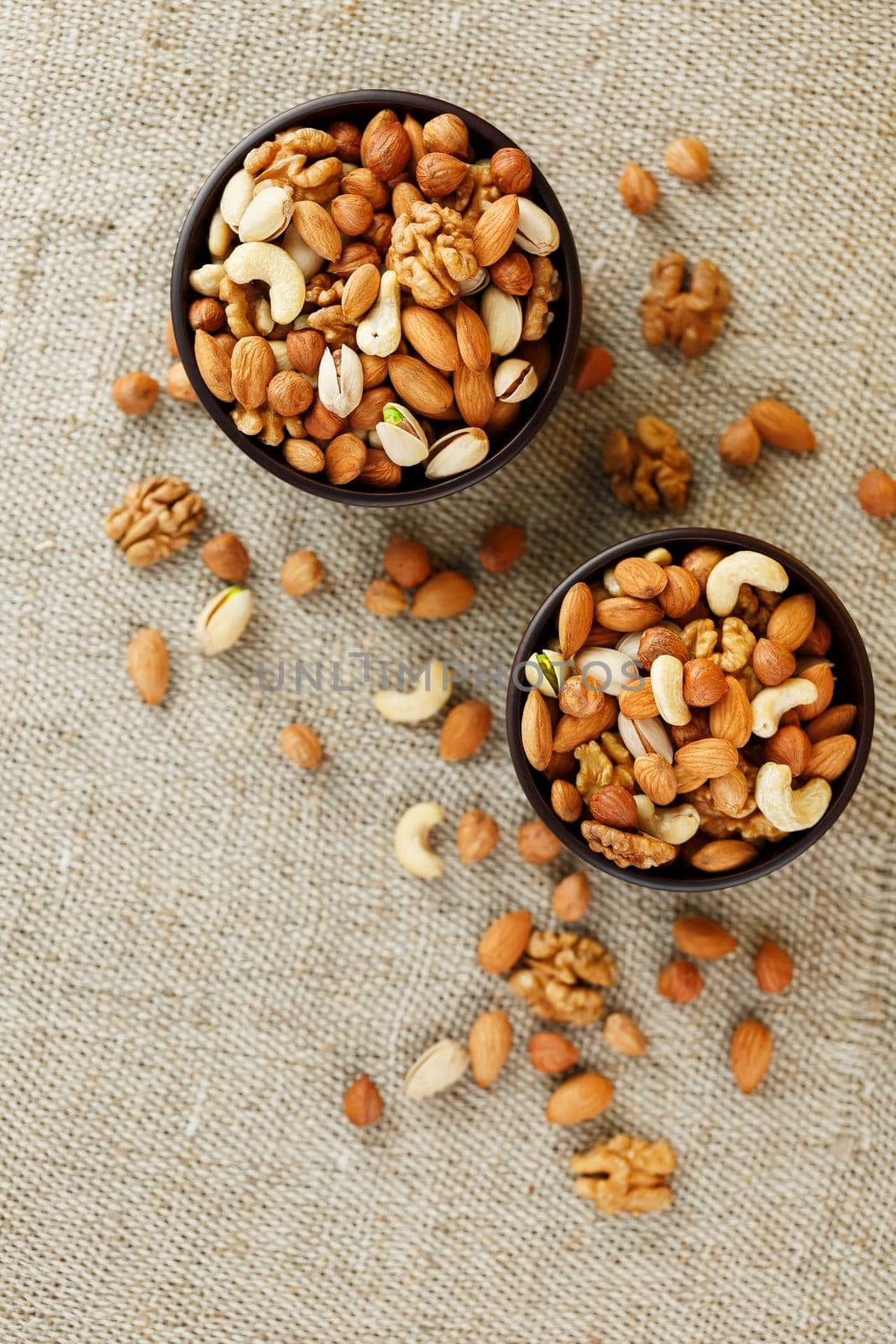 A mixture of cashew nuts, almond nuts, pistachios, hazelnuts and walnuts in a wooden cup against the background of burlap fabric. Nuts as structure and background, macro. Two cups of nuts.