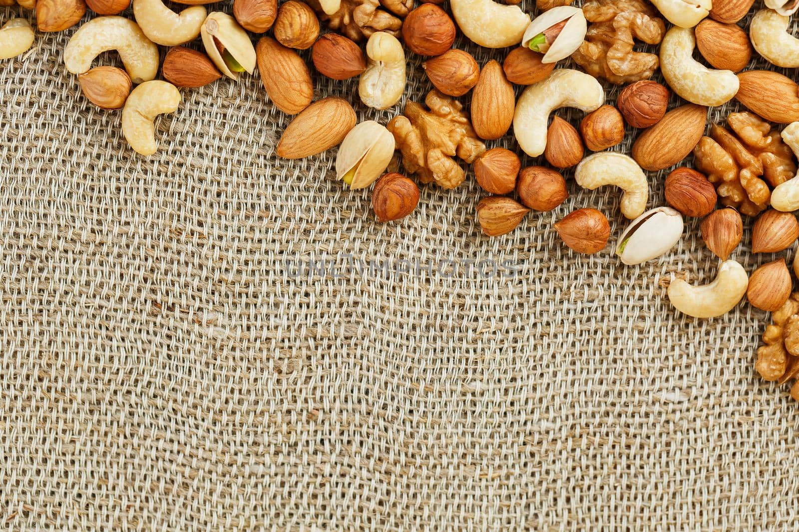 Mix of nuts of cashew, almonds, pistachios, hazelnuts and walnuts is against the background of brown fabric of burlap. Nuts as structure and background, macro