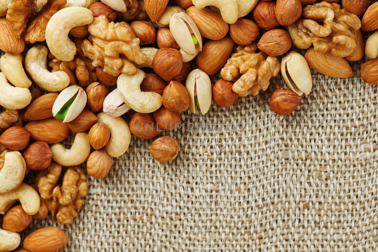 Mix of nuts of cashew, almonds, pistachios, hazelnuts and walnuts is against the background of brown fabric of burlap. Nuts as structure and background, macro