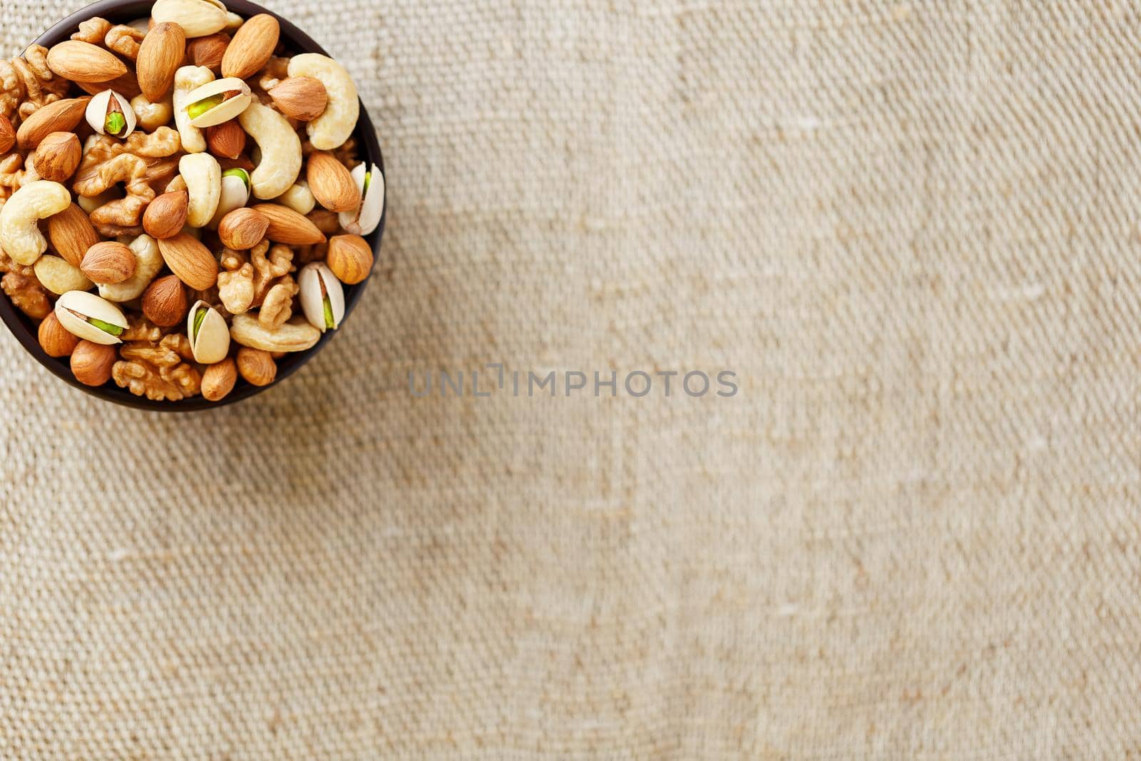 Mix of nuts of cashew, almonds, pistachios, hazelnuts and walnuts is against the background of brown fabric of burlap. Nuts as structure and background, macro