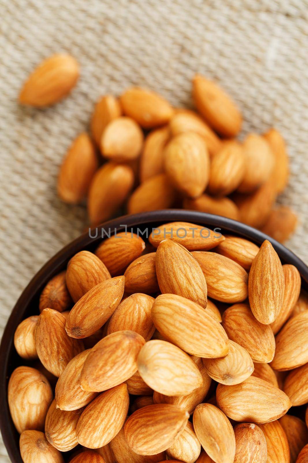 Almonds in a wooden cup on a burlap cloth background. Golden almond closeup in dark brown cup