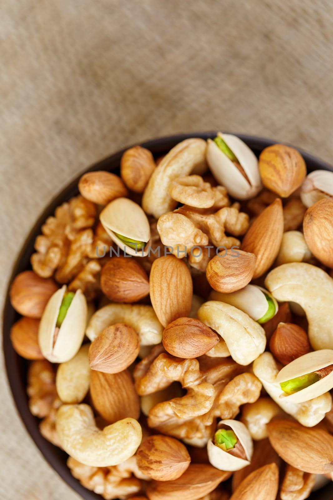 Mix of nuts of cashew, almonds, pistachios, hazelnuts and walnuts is against the background of brown fabric of burlap. Nuts as structure and background, macro