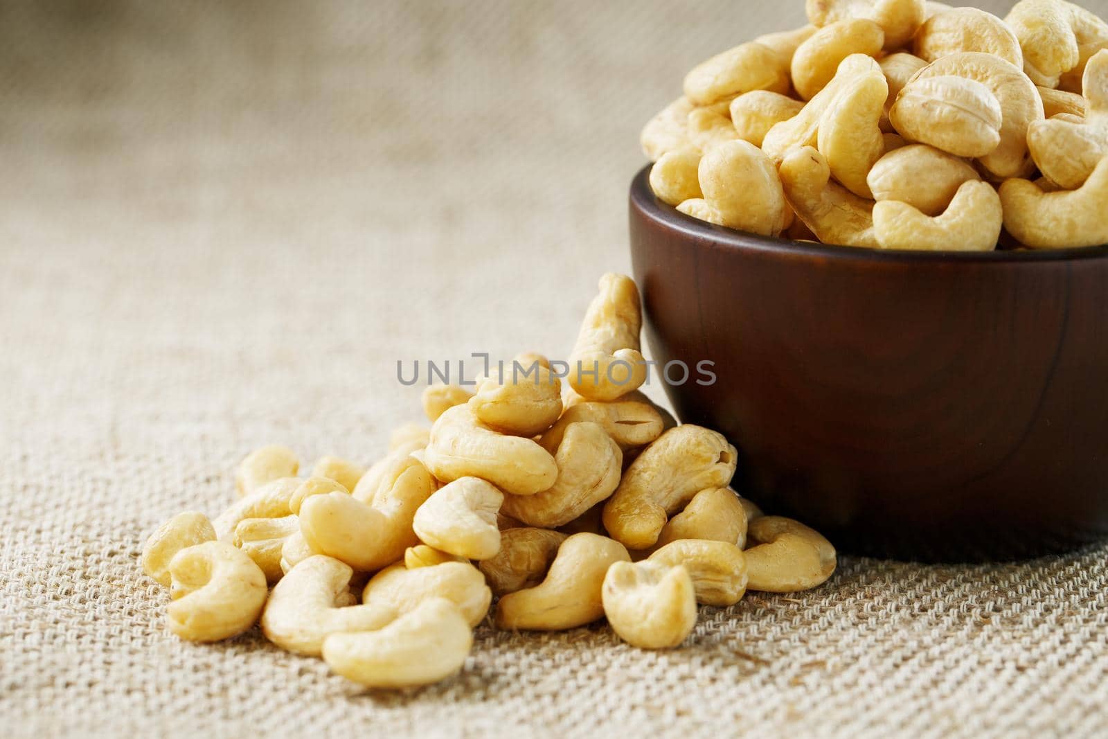 Cashew nuts in a wooden bowl on a burlap cloth background. Golden cashew close-up in a dark brown cup.