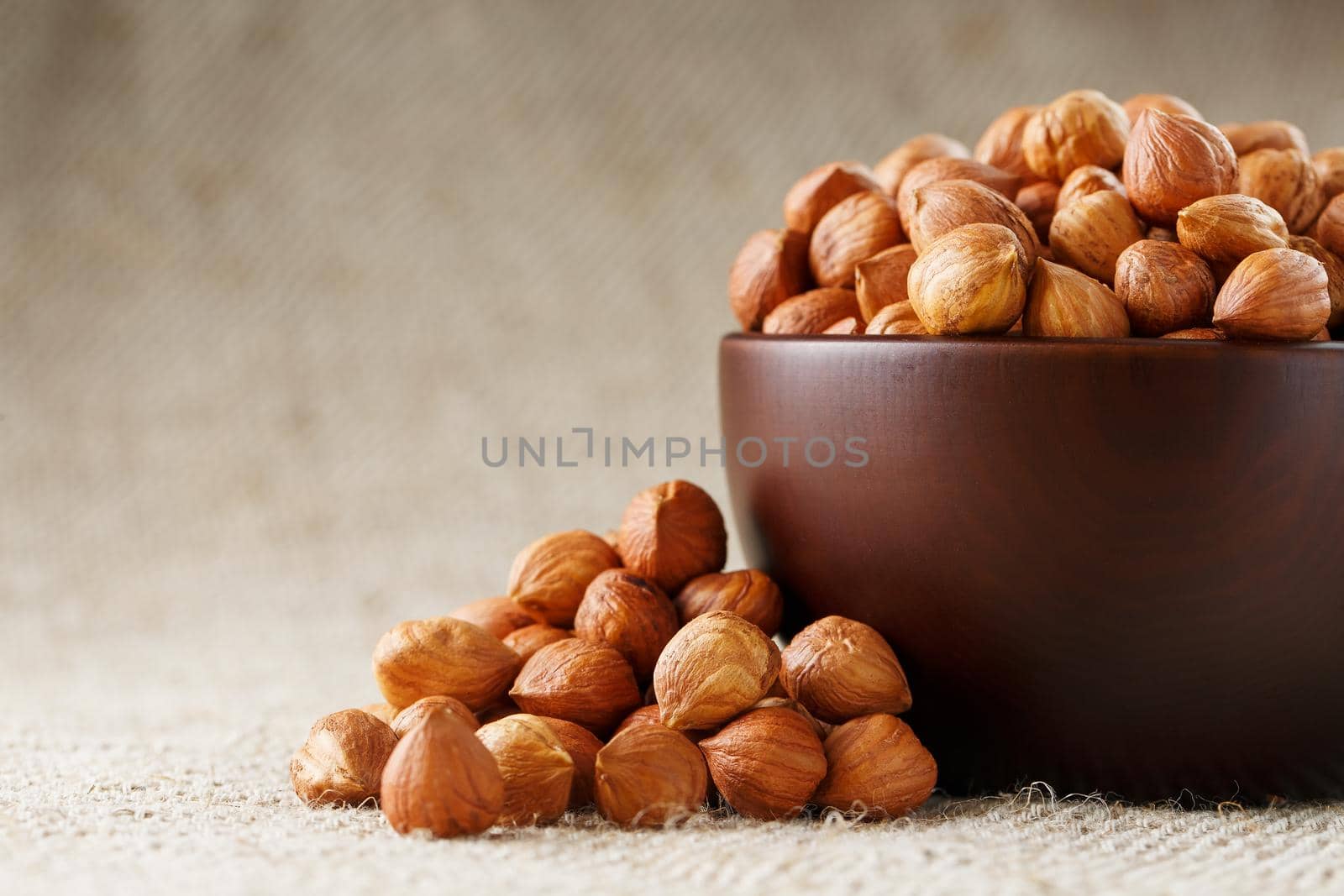 Peeled hazelnuts in a wooden, dark brown cup on a burlap cloth. Super Food, Raw. View from above.