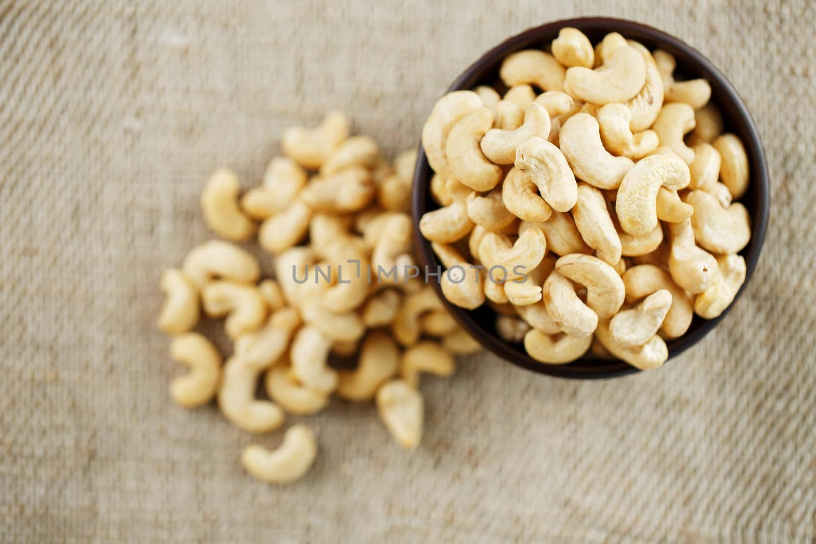 Cashew nuts in a wooden bowl on a burlap cloth background. Golden cashew close-up in a dark brown cup.