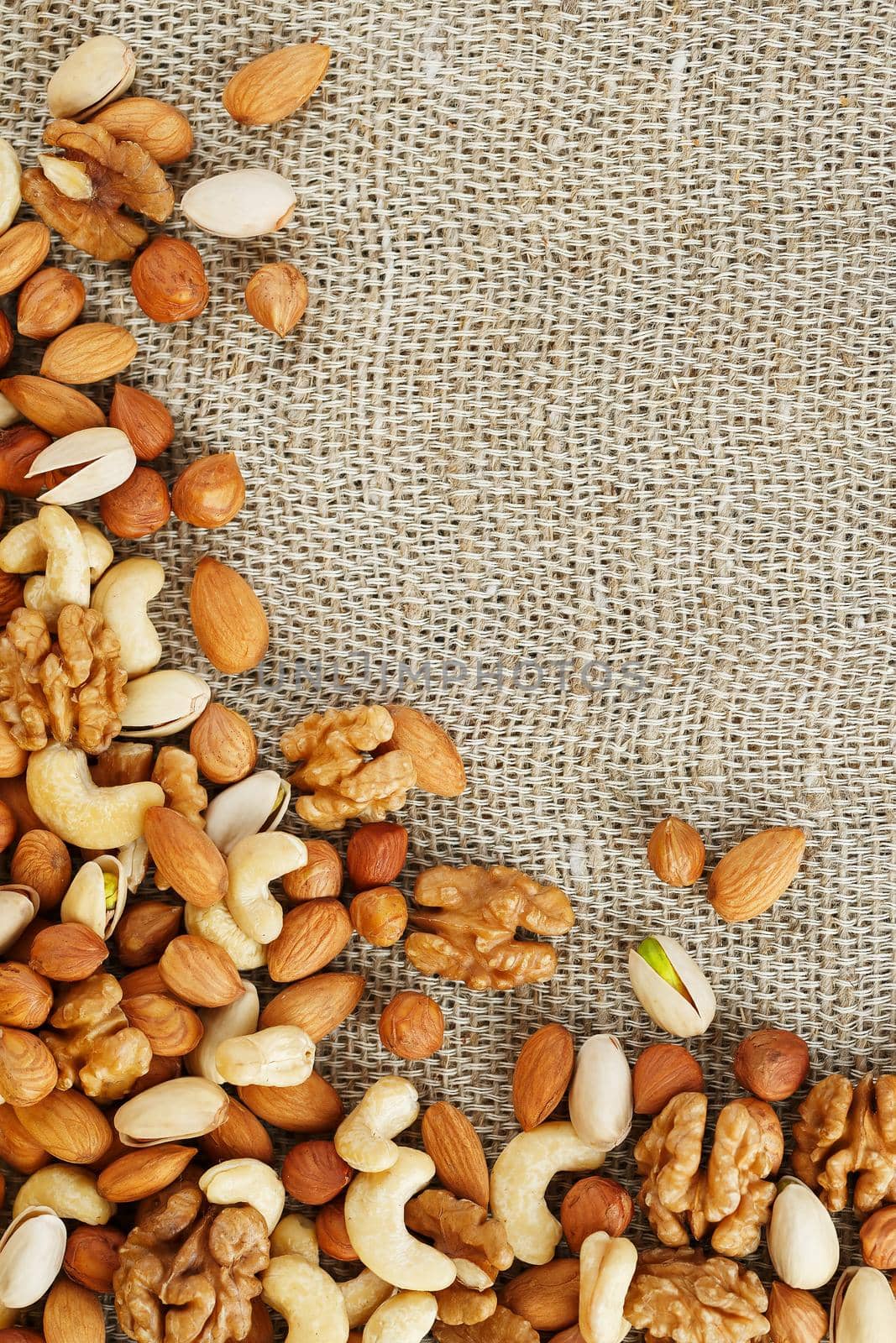 Mix of nuts of cashew, almonds, pistachios, hazelnuts and walnuts is against the background of brown fabric of burlap. Nuts as structure and background, macro