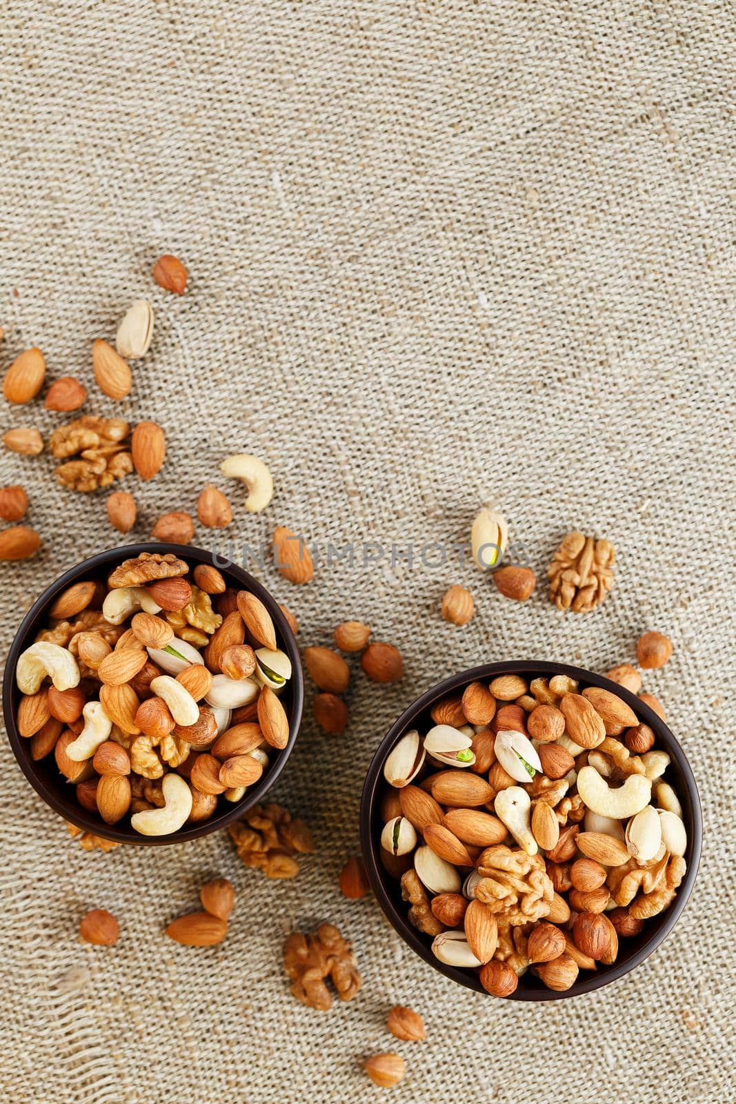 A mixture of cashew nuts, almond nuts, pistachios, hazelnuts and walnuts in a wooden cup against the background of burlap fabric. Nuts as structure and background, macro. Two cups of nuts.