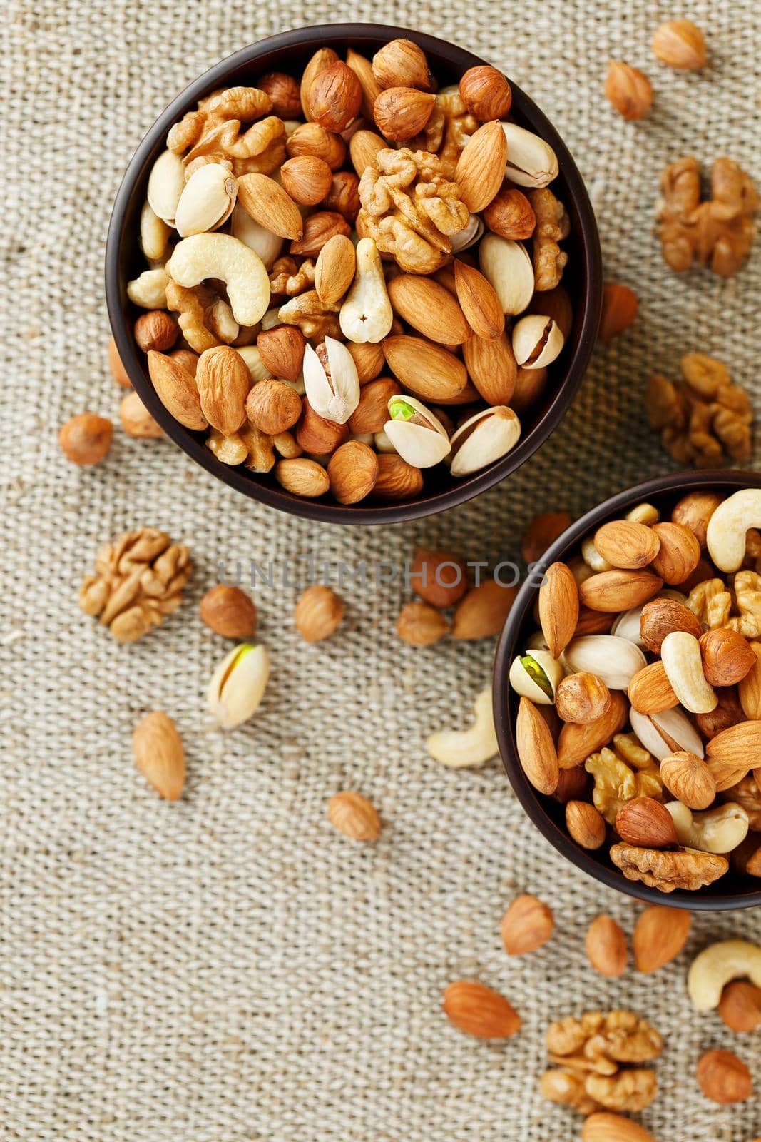 A mixture of cashew nuts, almond nuts, pistachios, hazelnuts and walnuts in a wooden cup against the background of burlap fabric. Nuts as structure and background, macro. Two cups of nuts.