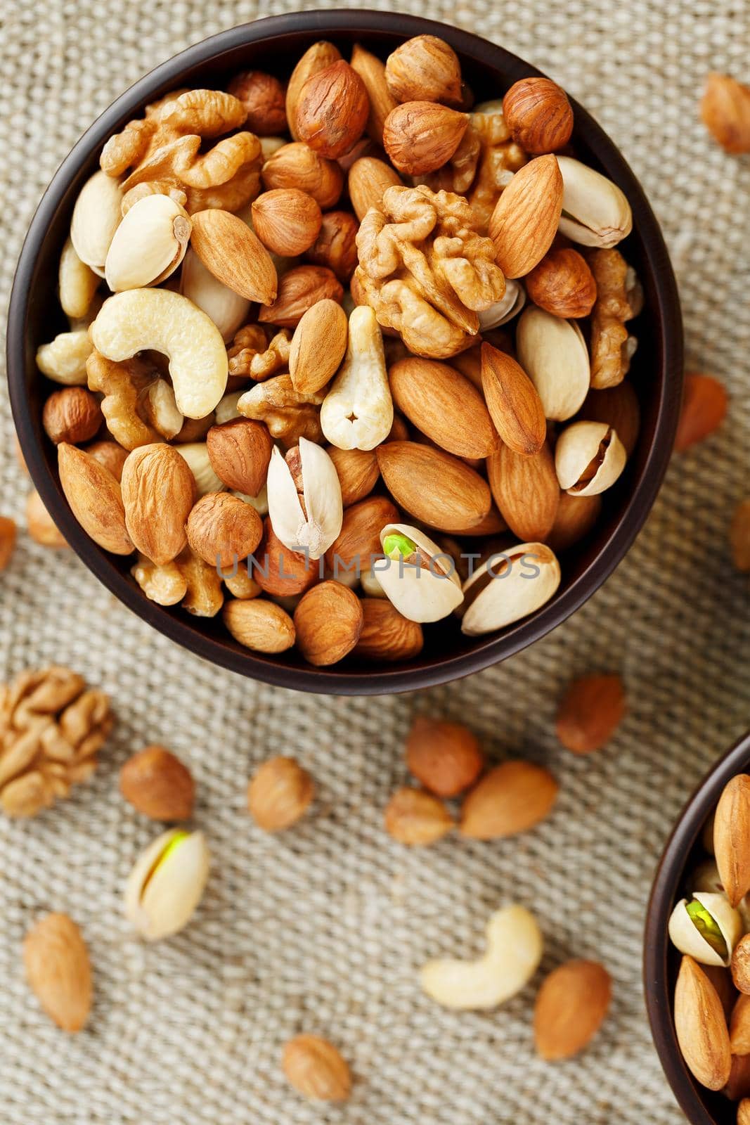 A mixture of cashew nuts, almond nuts, pistachios, hazelnuts and walnuts in a wooden cup against the background of burlap fabric. Nuts as structure and background, macro. Two cups of nuts.