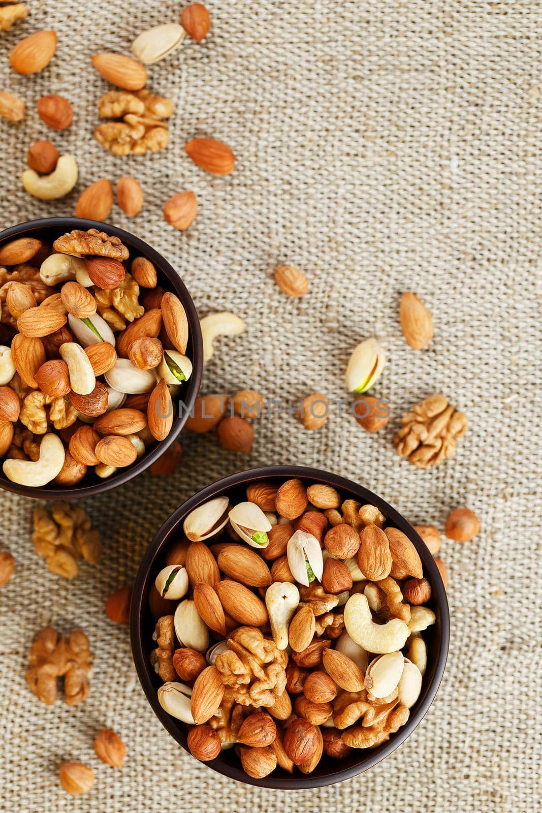 A mixture of cashew nuts, almond nuts, pistachios, hazelnuts and walnuts in a wooden cup against the background of burlap fabric. Nuts as structure and background, macro. Two cups of nuts.