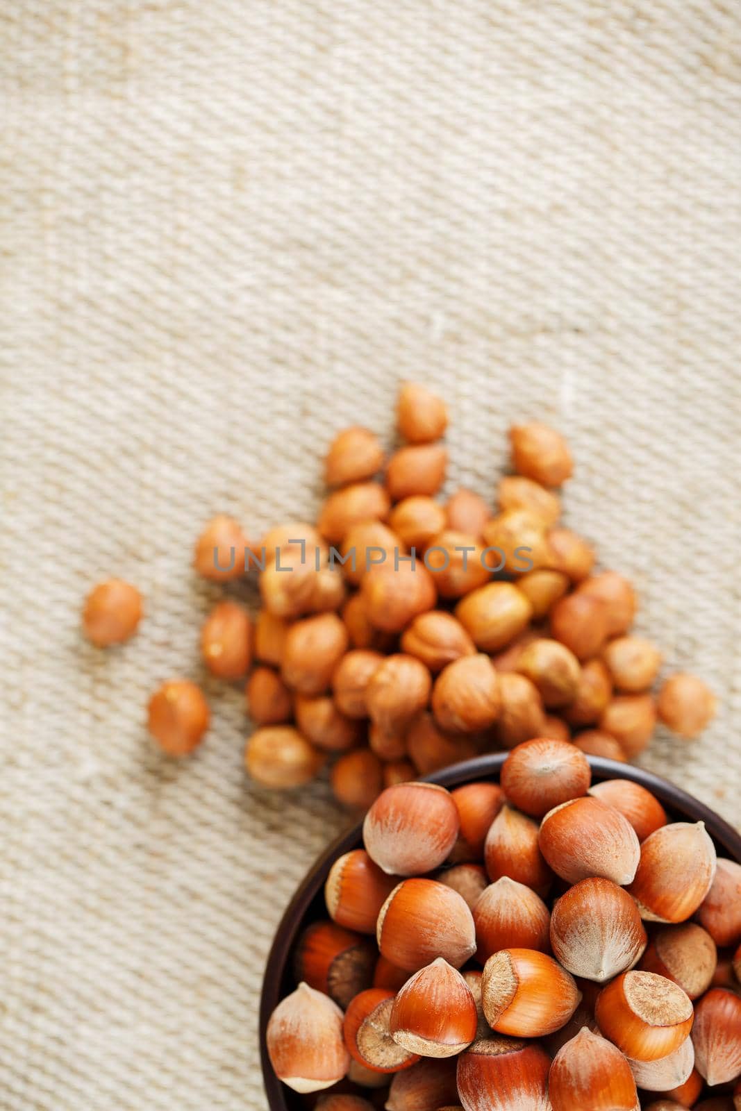 Peeled hazelnuts in a wooden, dark brown cup on a burlap cloth. Super Food, Raw. View from above.