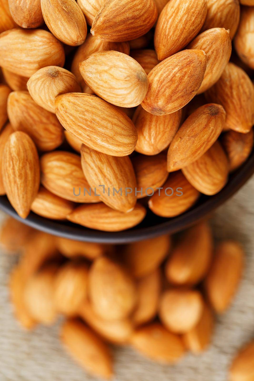 Almonds in a wooden cup on a burlap cloth background. Golden almond closeup in dark brown cup