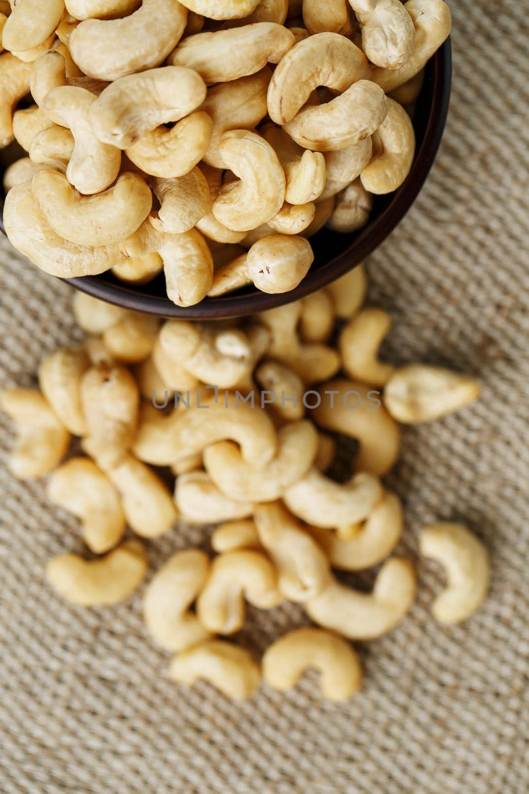 Cashew nuts in a wooden bowl on a burlap cloth background. Golden cashew close-up in a dark brown cup.