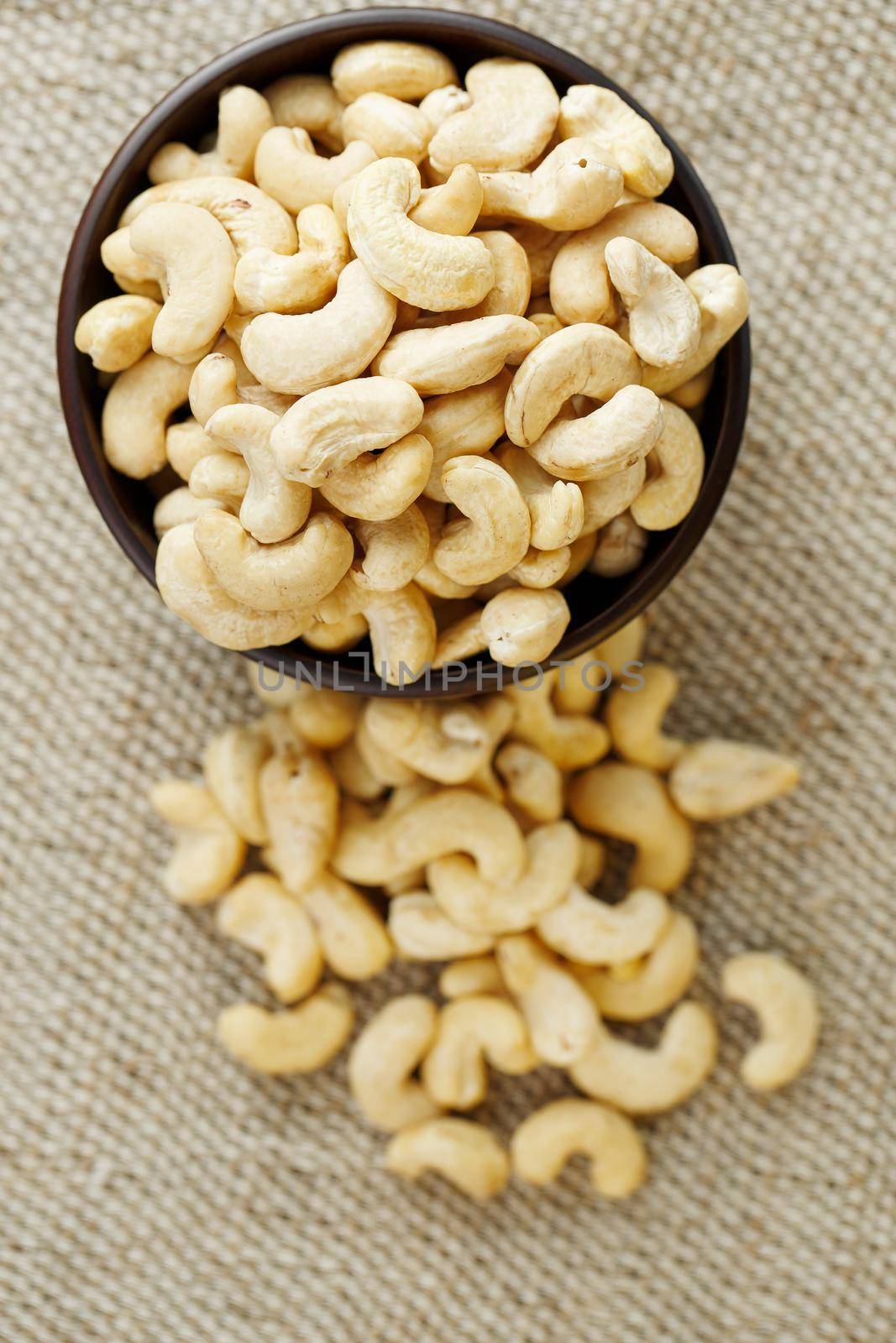 Cashew nuts in a wooden bowl on a burlap cloth background. Golden cashew close-up in a dark brown cup.