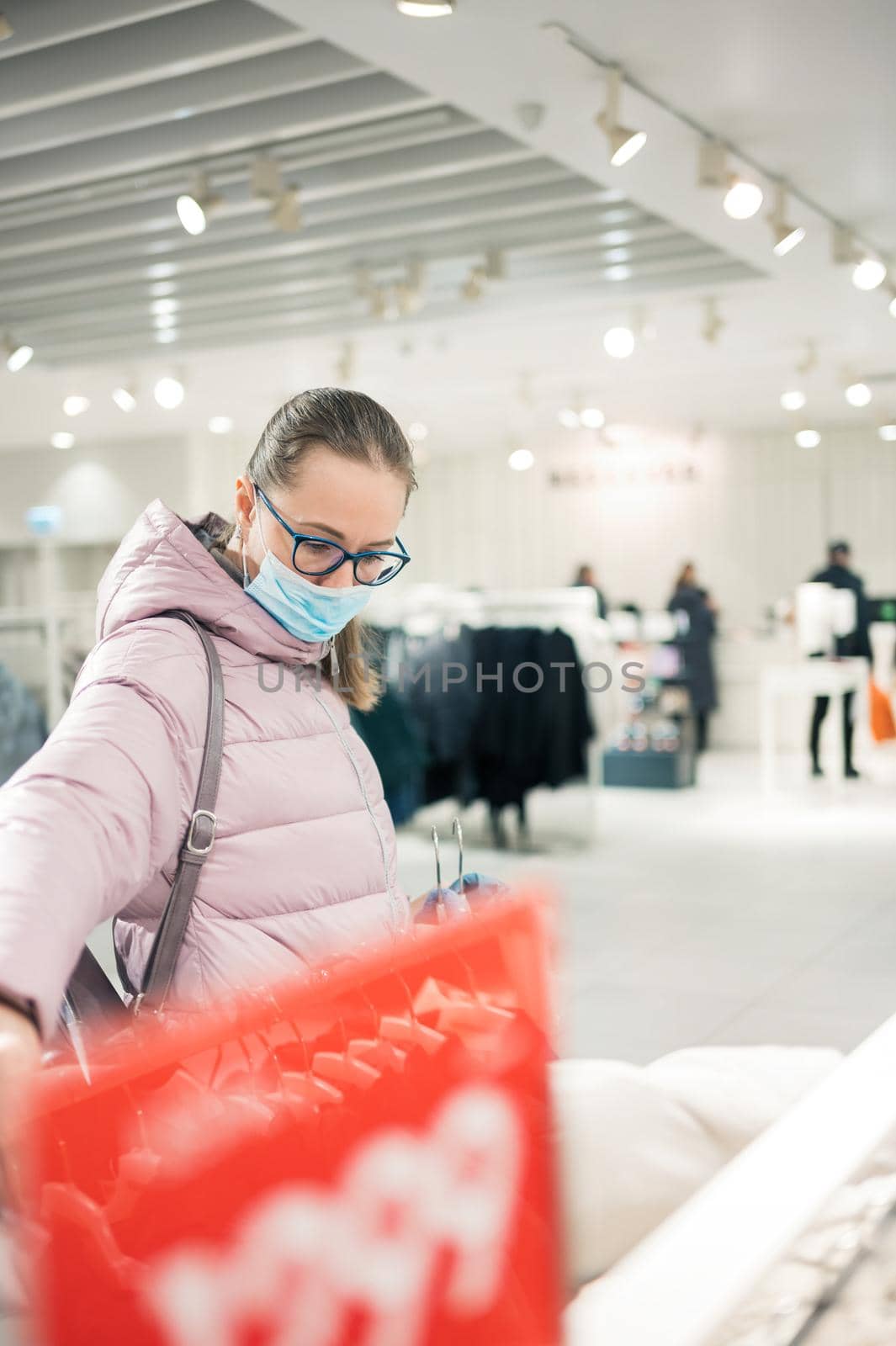 Woman wearing protective face mask shopping clothes in retail shopping store. Concept of lifestyle during corona virus pandemic.
