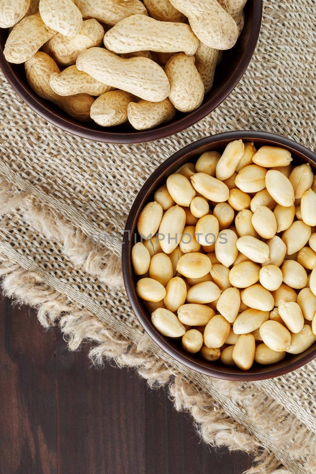 Peanuts in the shell and peeled close up in a cup. Background with peanuts. Roasted peanuts in the shell and peeled on a background of brown cloth in cups