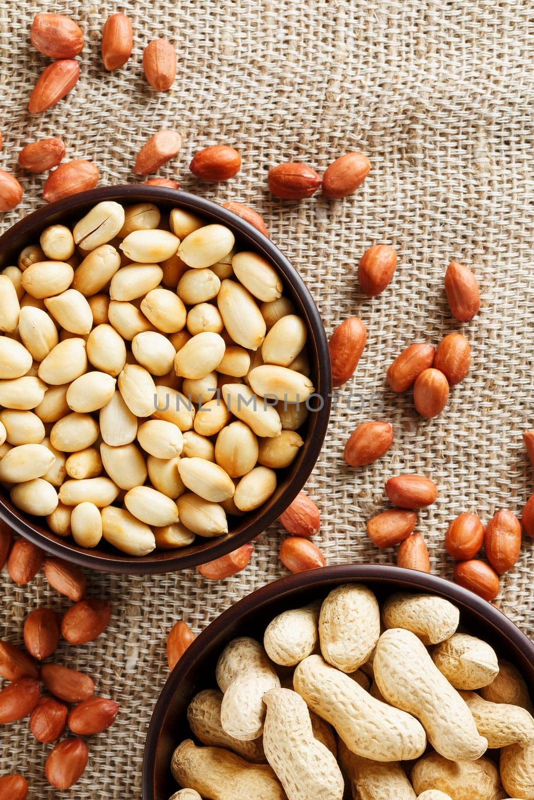 Peanuts in the shell and peeled closeup in a cup. Background with peanuts. Roasted peanuts in the shell and peeled on a background of brown cloth in cups