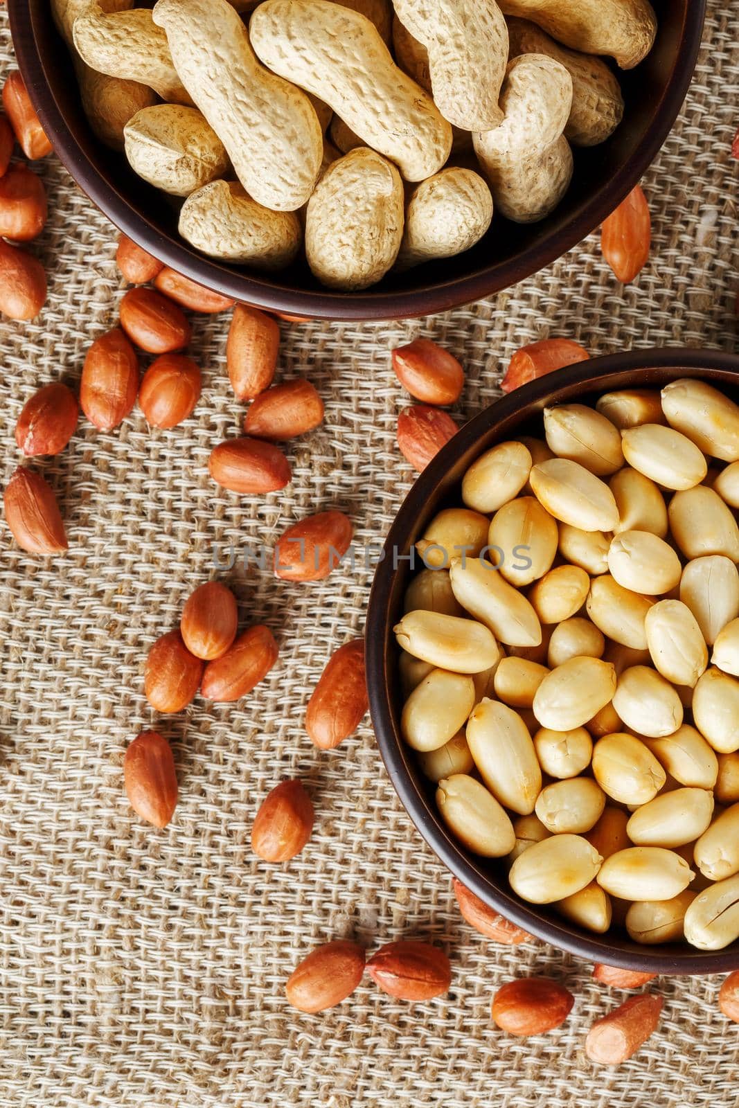 Peanuts in the shell and peeled closeup in a cup. Background with peanuts. Roasted peanuts in the shell and peeled on a background of brown cloth in cups