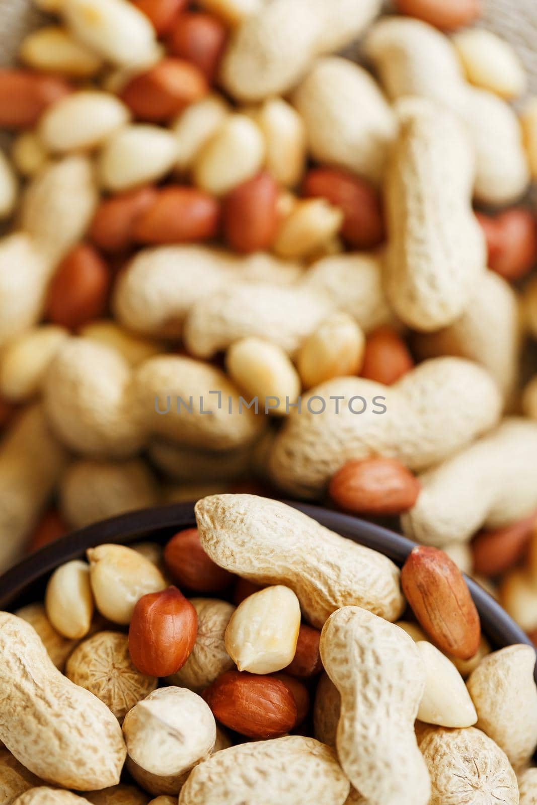 Peanuts in the shell and peeled close up in a cup. Background with peanuts. Roasted peanuts in the shell and peeled on a background of brown cloth in cups