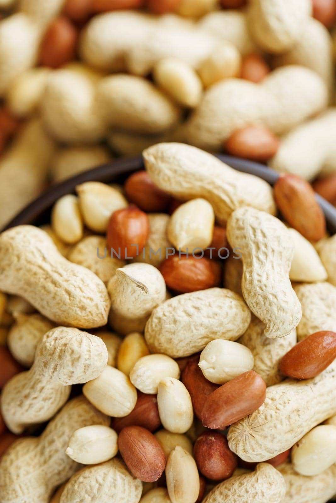 Peanuts in the shell and peeled close up in a cup. Background with peanuts. Roasted peanuts in the shell and peeled on a background of brown cloth in cups