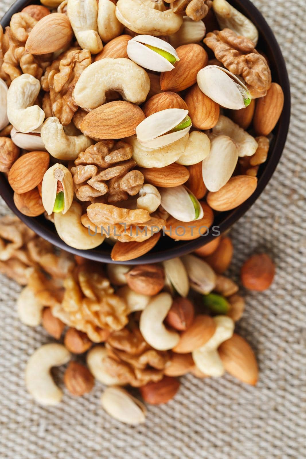 Mix of nuts of cashew, almonds, pistachios, hazelnuts and walnuts is against the background of brown fabric of burlap. Nuts as structure and background, macro