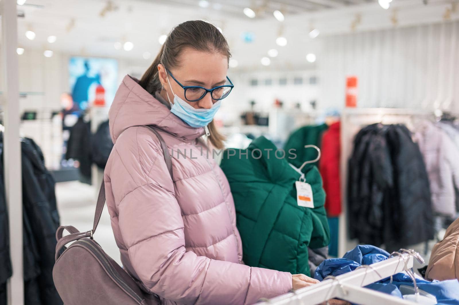 Woman wearing protective face mask shopping clothes in retail shopping store. Concept of lifestyle during corona virus pandemic.