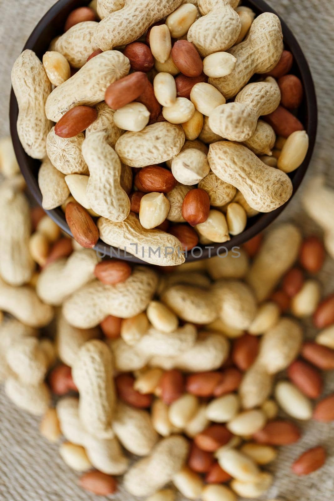 Peanuts in the shell and peeled close up in a cup. Background with peanuts. Roasted peanuts in the shell and peeled on a background of brown cloth in cups