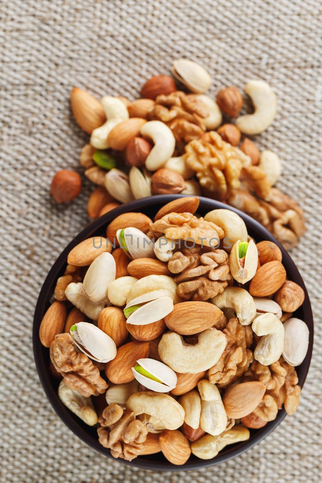 Mix of nuts of cashew, almonds, pistachios, hazelnuts and walnuts is against the background of brown fabric of burlap. Nuts as structure and background, macro