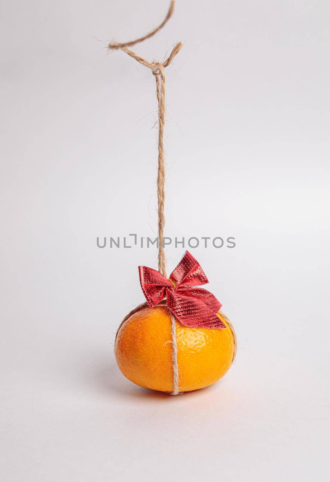 Festive tangerine with a red bow hanging from a rope. Holiday concept New Year.