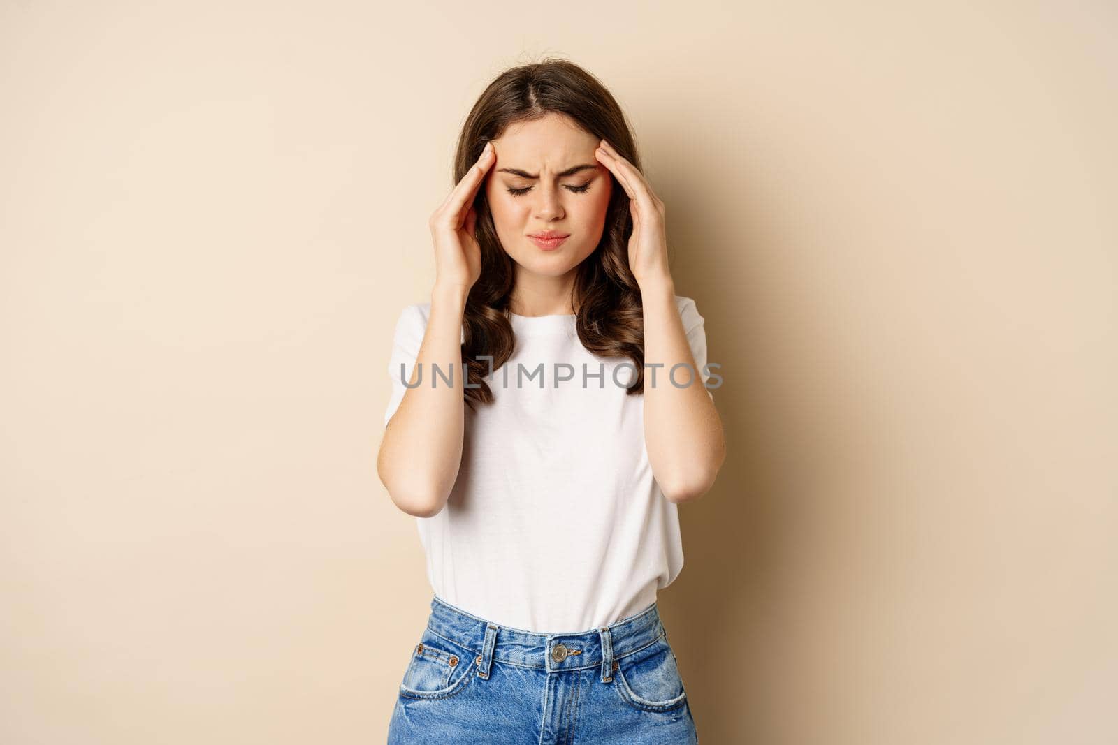 Health and women concept. Portrait of girl feeling sick, touching head temples, feeling headache, migraine, standing over beige background by Benzoix