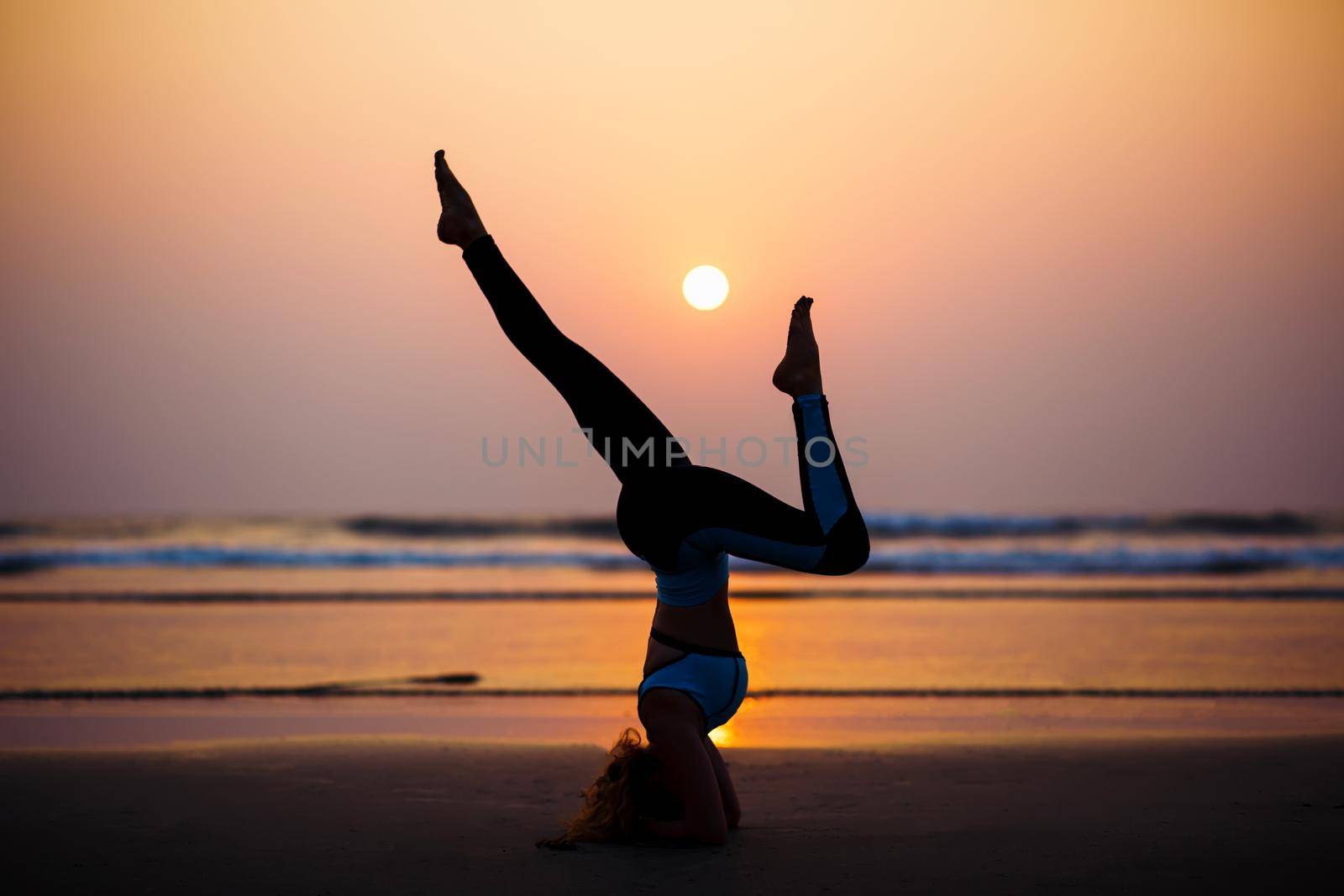 Young healthy woman practicing yoga on the beach at sunset