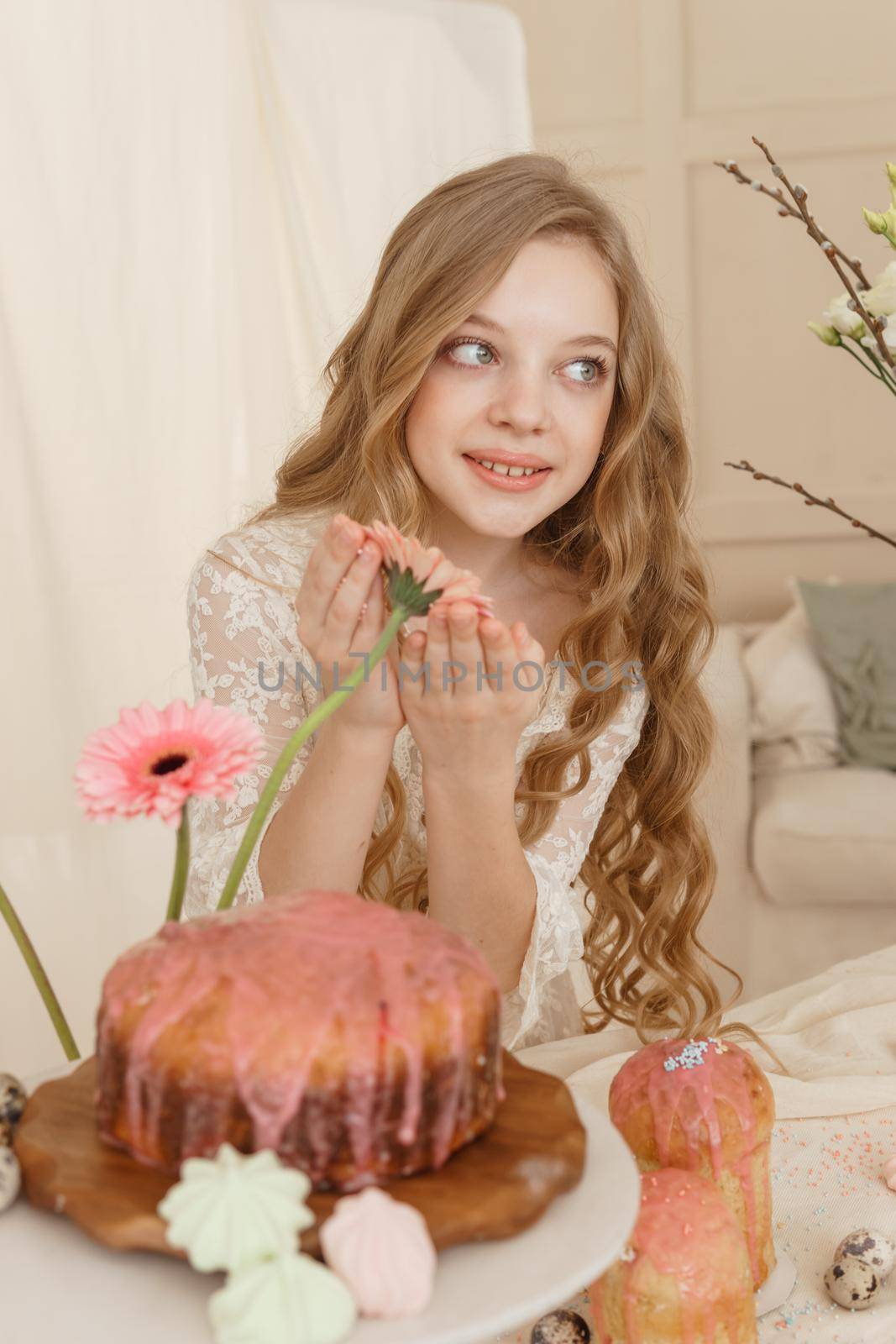 A girl with long hair in a light dress is sitting at the Easter table with cakes, spring flowers and quail eggs. Happy Easter celebration