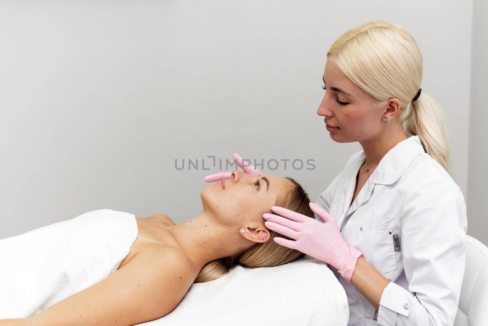 Young beautician or dermatologist doing manual facial cleansing for a woman in a beauty salon. Spa facial massage. Beautiful woman receiving facial massage in a beauty salon. The beautician makes cosmetic procedures to a female client.