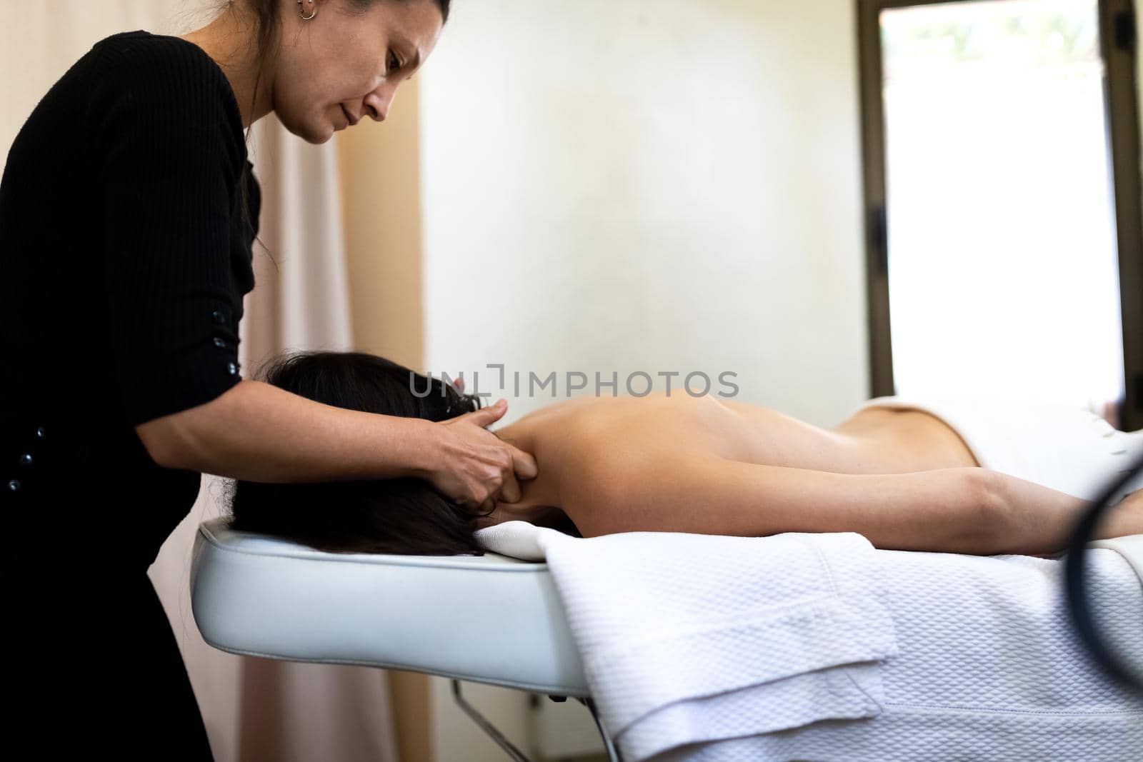 Side view of latina massage therapist giving neck massage to female client. Copy space. Spa treatment and wellness concept.