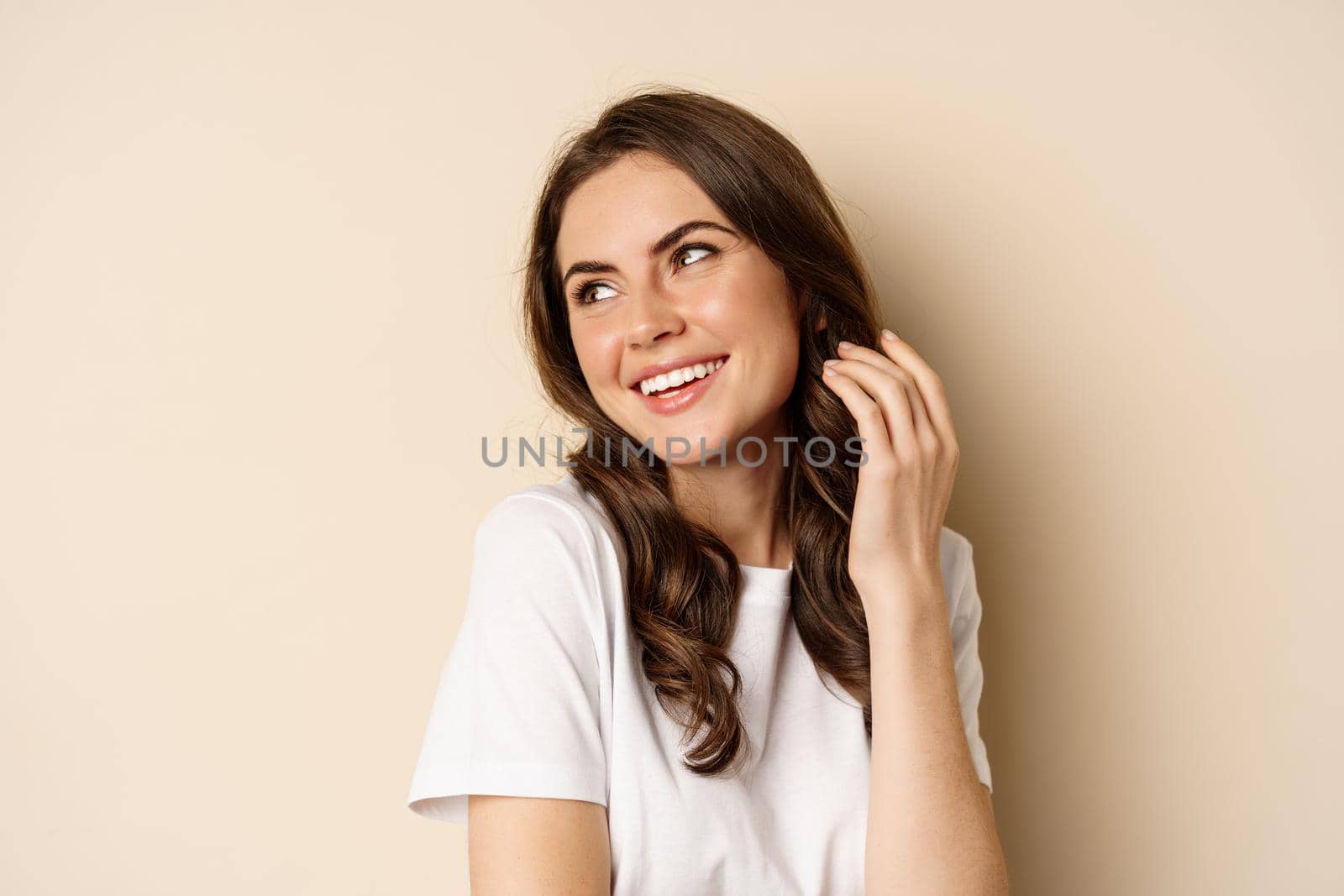 Close up portrait of coquettish beautiful girl gazing silly, gently smiling and giggling, posing flirty and cute against beige background. Women beauty and valentines concept.