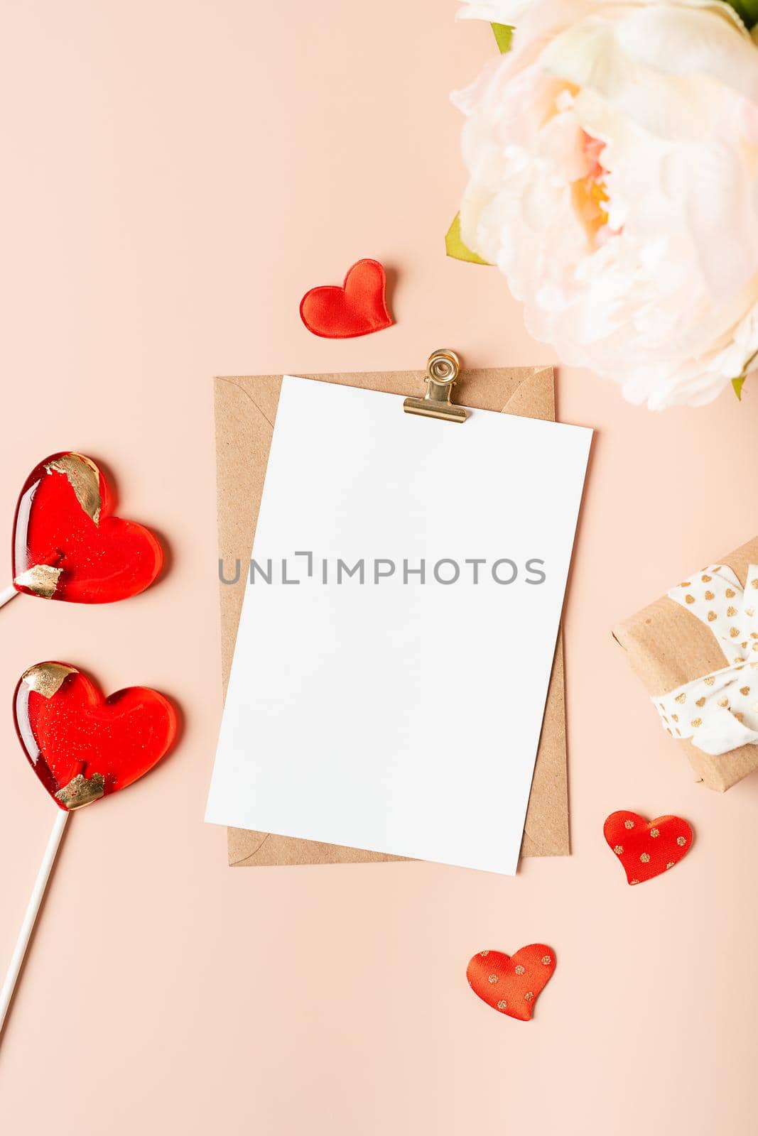 Flat lay of paper envelope with blank mockup greeting paper card. Pink table background with Valentine day gift, letter, heart shape, flowers, lollipops and decoration. Top view, mock up invitations