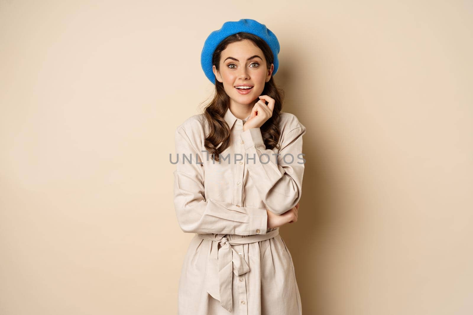 Image of stylsh beautiful woman looking surprised, shocked reaction at camera, posing in trench coat against beige background by Benzoix