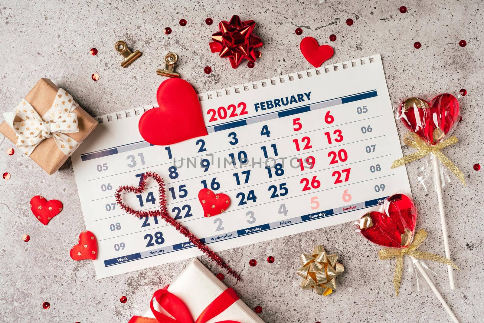 Flat lay of Valentines day calendar composition. Top view Gifts, paper, hearts confetti, ribbon, lollipops on grey table background. 14th February love concept.