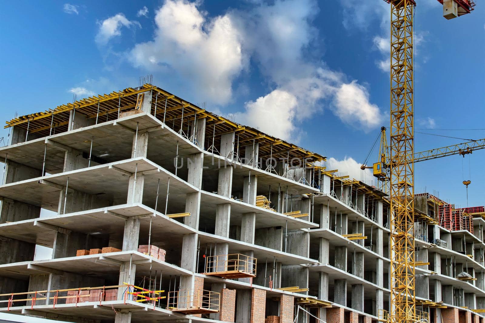 Frame of a new residential building under construction. New building. Concrete panels. Mounting cranes at a construction site. Real estate under construction. Housing investment. Blue sky with clouds.