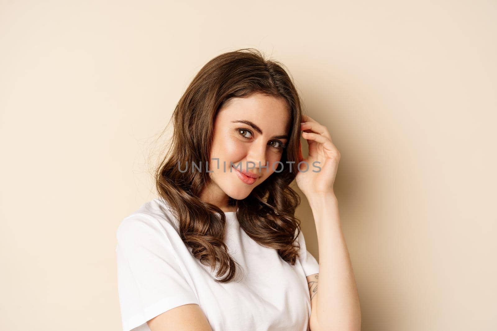 Close up portrait of coquettish beautiful girl gazing silly, gently smiling and giggling, posing flirty and cute against beige background. Women beauty and valentines concept by Benzoix