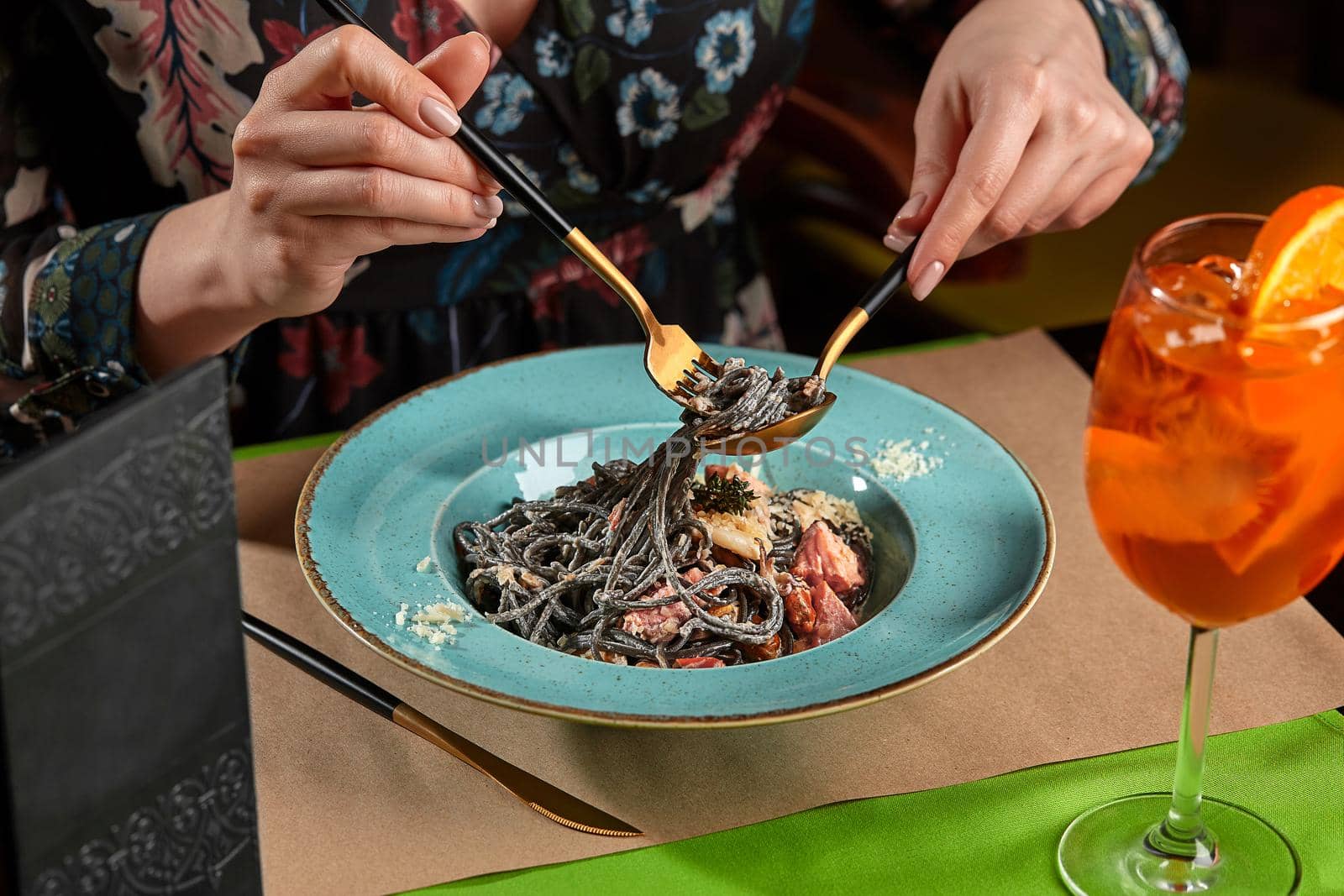 Cropped shot of woman eating black pasta with seafood served with orange spritz by nazarovsergey