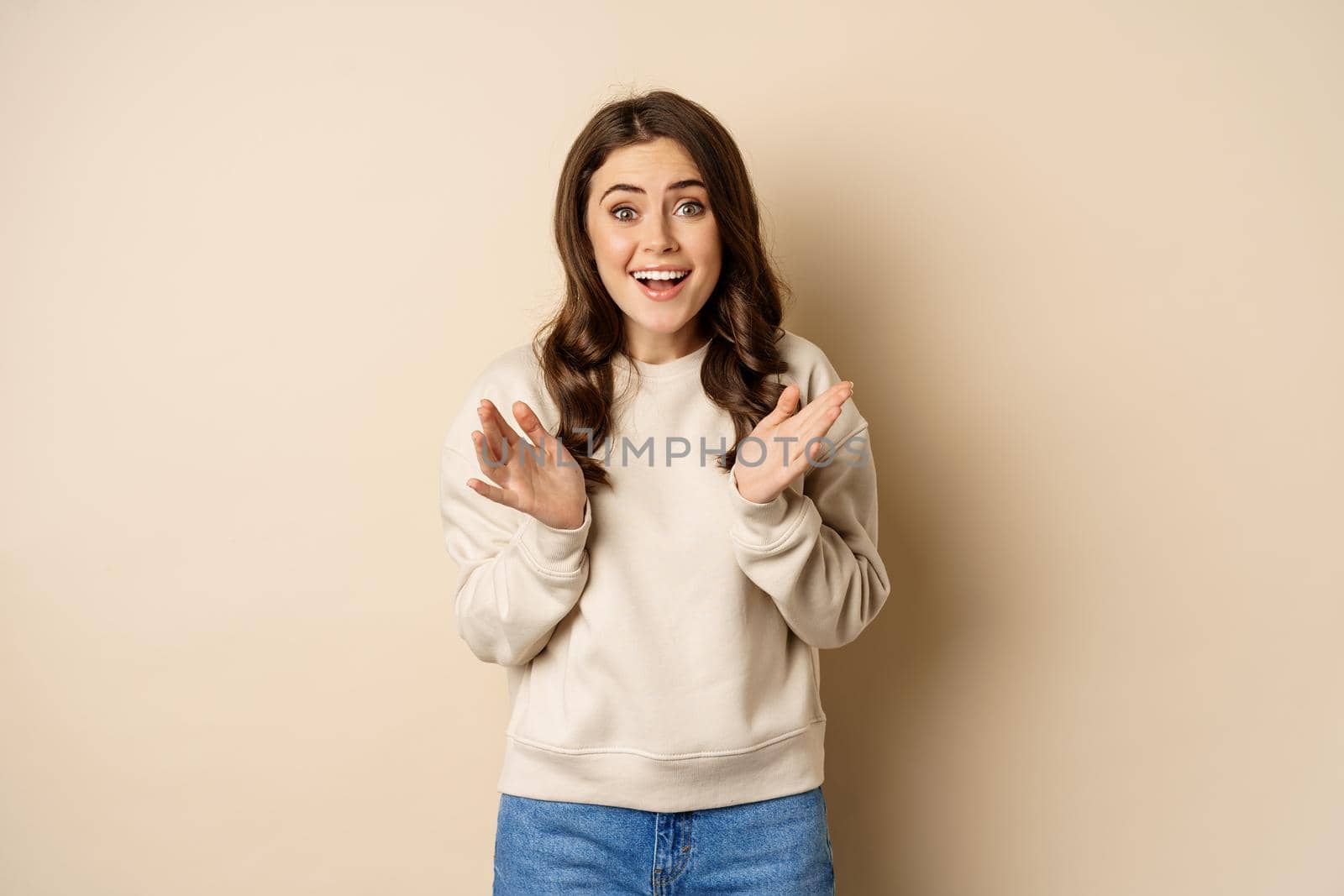 Image of surprised, amazed brunette girl gasping, looking fascinated at camera, standing over beige background by Benzoix