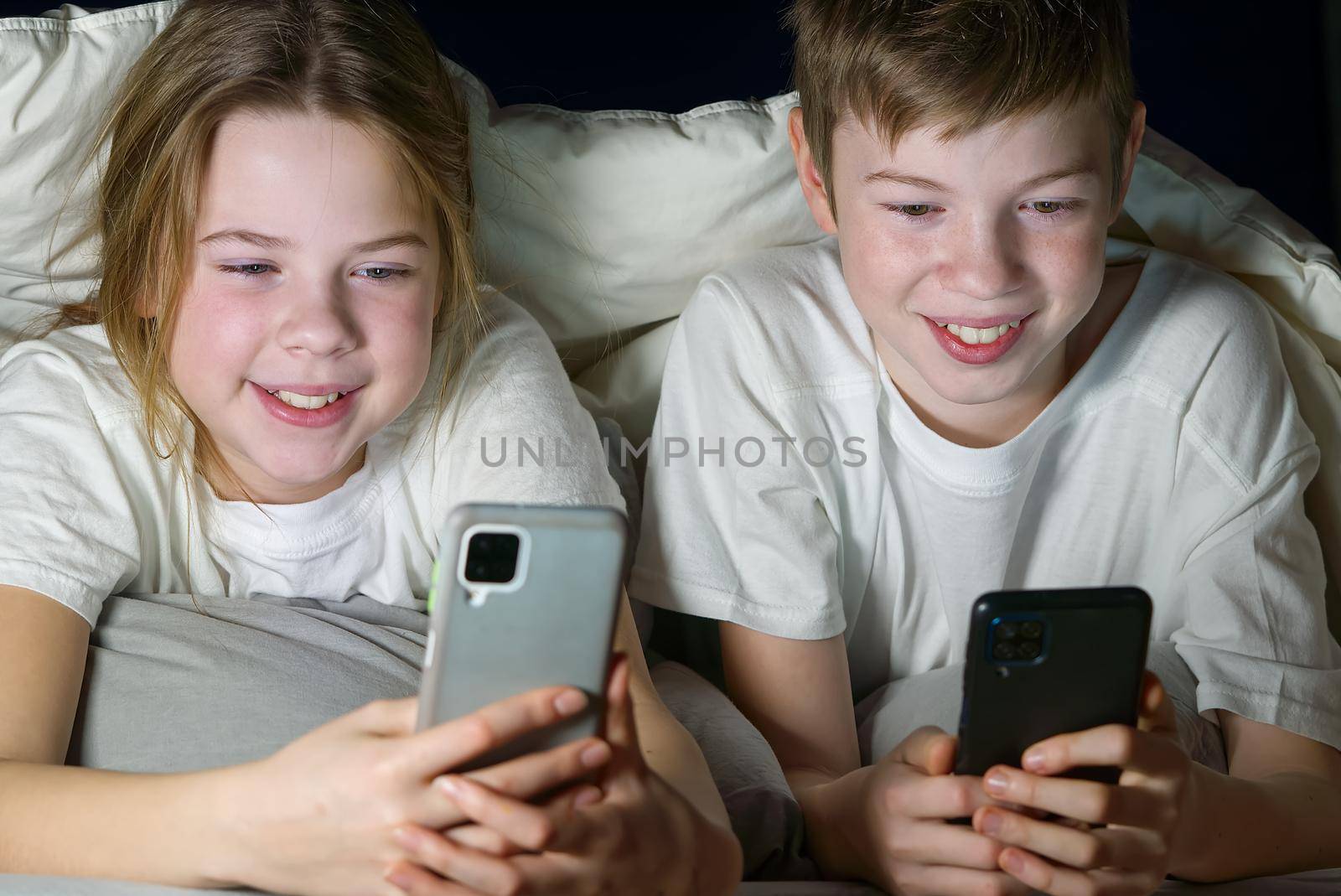 children play games on a smartphone or tablet at night under a blanket, rewrites with friends on social networks. social media addiction by PhotoTime