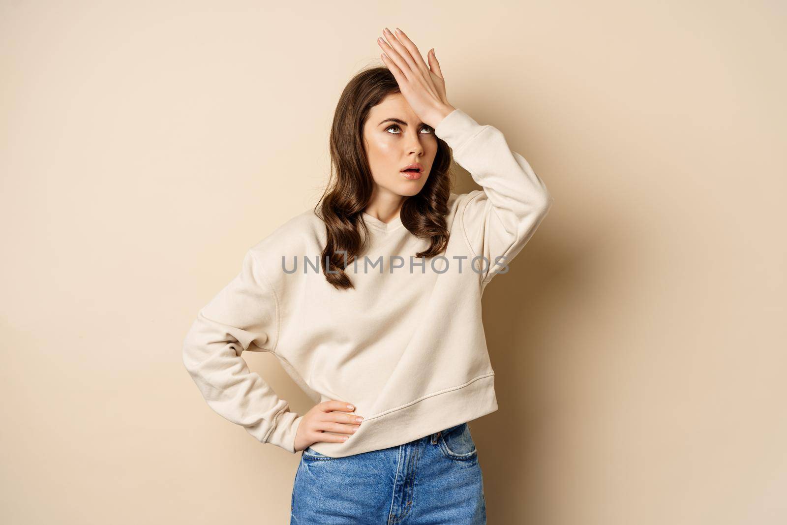 Annoyed woman facepalm, roll eyes irritated, bothered by smth stupid, standing over beige background.