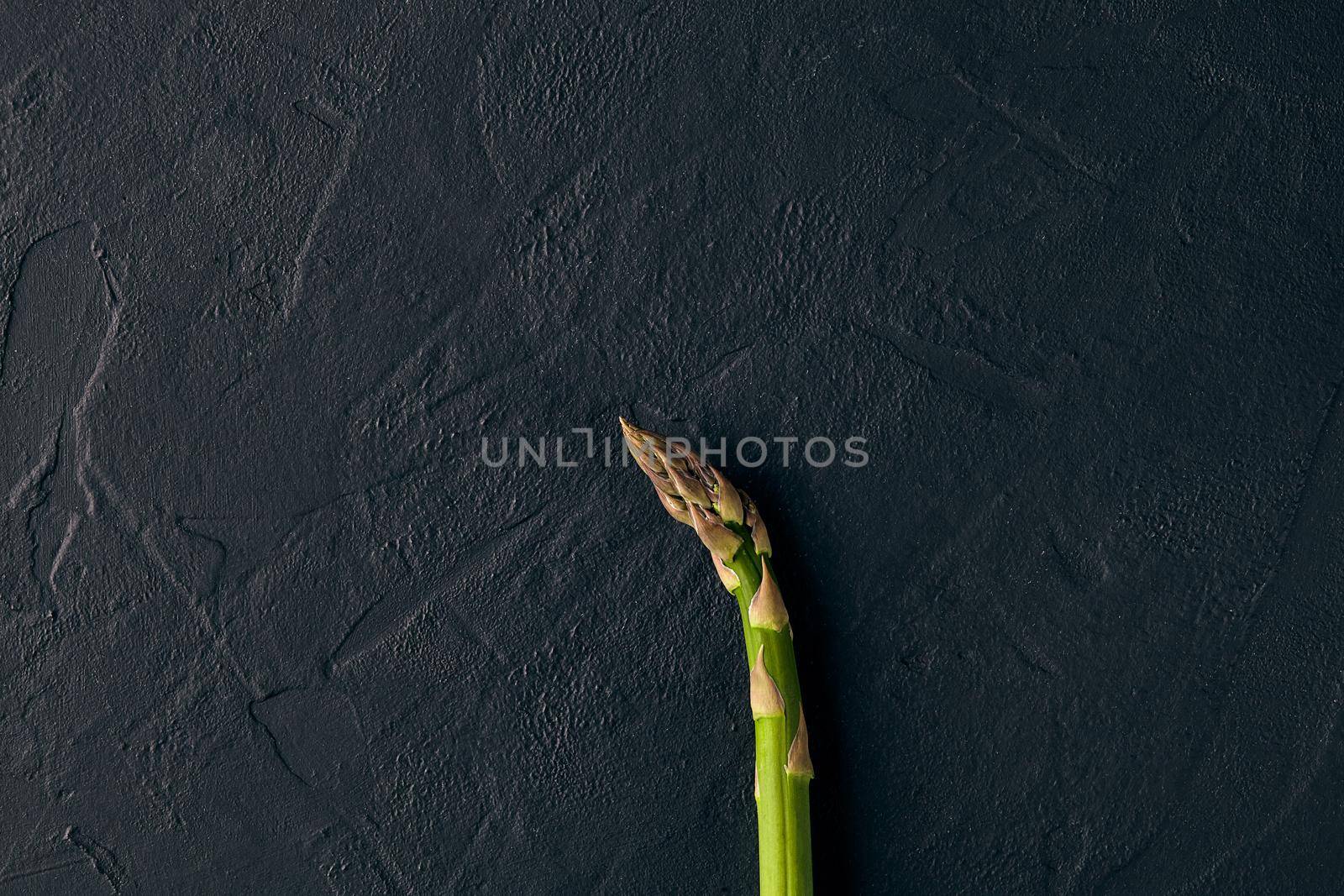 One raw fresh green asparagus stalk over black slate background. Concept of food and seasonal vegetables crop. Close up, copy space. Flat lay, top view