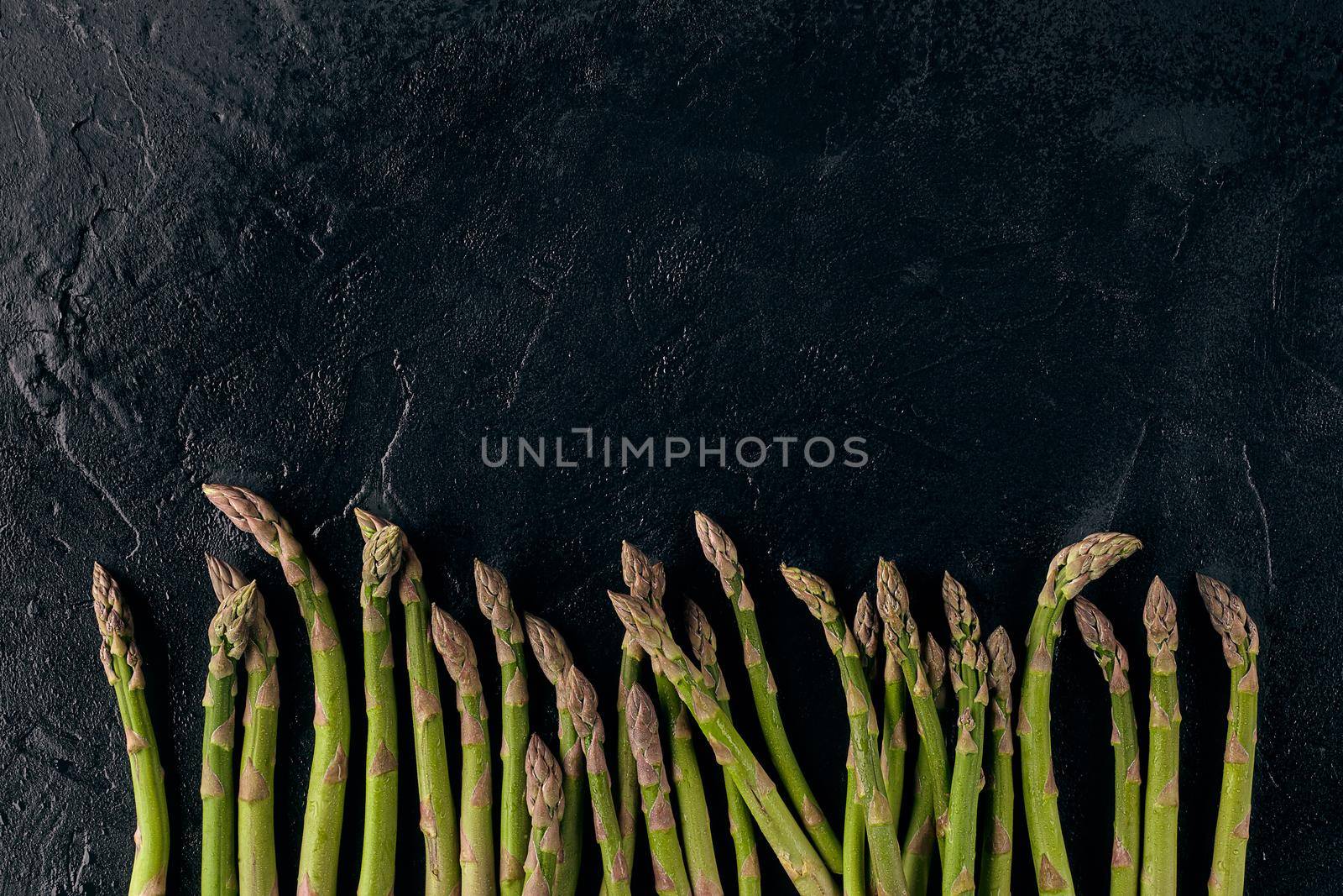 Raw uncooked green asparagus spears on black slate background. Concept of healthy nutrition, food and seasonal vegetables harvest. Close up, copy space. Flat lay, top view